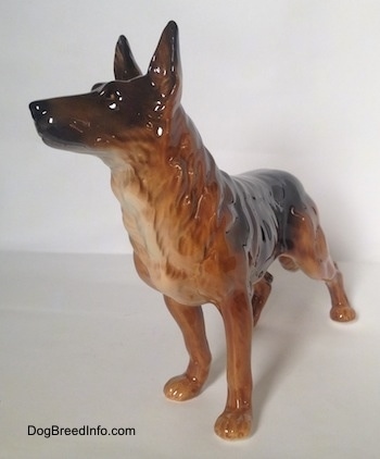The front left side of a brown with black standing German Shepherd figurine. The figurine has its ears in the air.