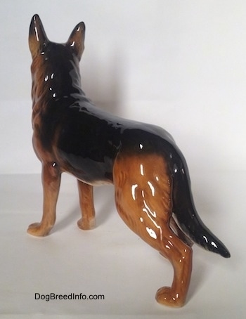 The back left side of a brown with black German Shepherd standing figurine. The figurine has a tail that goes down the length of its legs.