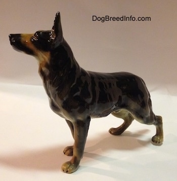 The front left side of a figurine of a black with tan German Shepherd standing figurine. The figurine has its ears alert in the air.