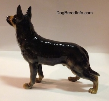 The left side of a black with tan figurine of a standing German Shepherd. The figurine has a glossy side.