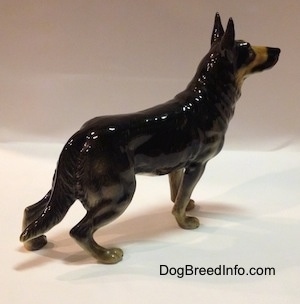 A black with tan figurine of a German Shepherds right side. The figurine has long legs.
