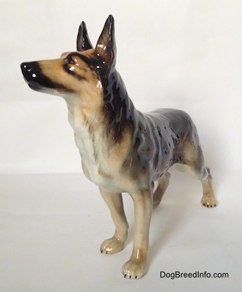 The front left side of a black and grey standing German Shepherd figurine. The figurine has its ears in the air.
