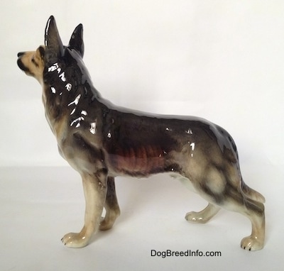 The left side of a black and grey figurine of a German Shepherd standing. The figurines body and legs are detailed.