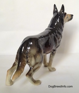 The back right side of a black and grey figurine of a standing German Shepherd.