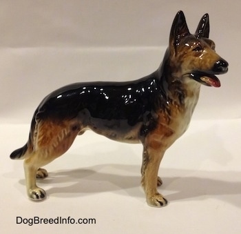 The right side of a porcelain black with brown and white German Shepherd figurine. The figurine has fine hair details along the side of its legs and chest.