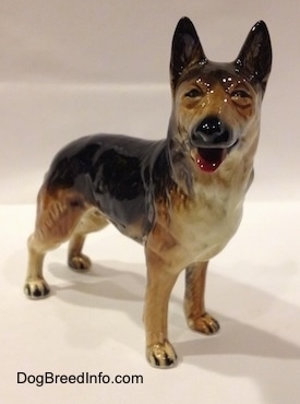 The front right side of a porcelain figurine of a black with brown and white standing German Shepherd. The figurine has squinty eyes.