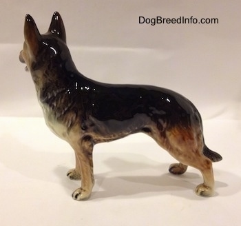 The left side of a porcelain black with brown and white German Shepherd standing figurine. The figurine has muscle details along its legs and body.