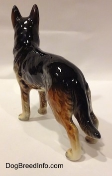 The back left side of a black with brown and white porcelain German Shepherd figurine. The figurine is glossy.