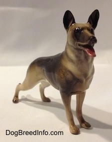 The front right side of a black with tan standing figurine of a German Shepherd. The figurine has its mouth painted open.