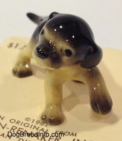 A figurine of a black with tan German Shepherd puppy standing. The puppy has its front left paw in the air.