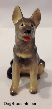 A figurine of a black with grey and tan German Shepherd sitting.