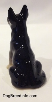 The back of a German Shepherd sitting figurine. The figurine has a tail circling around its right side.