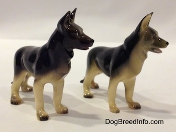 The front right side of two figurines of black with tan German Shepherds standing. The figurines have there mouths open.