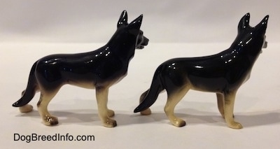 The right side of two black with tan figurine of a German Shepherd standing. The figurines have long legs.