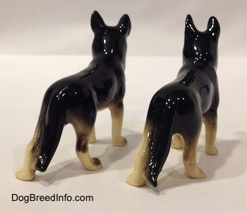 The back right side of two black with white figurines of German Shepherds standing. The figurines have glossy backs.