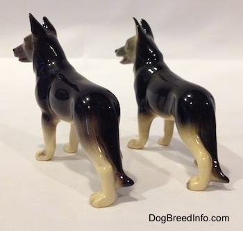 The back left side of two black with white German Shepherd standing figurines. The figurines tails are going down there legs.