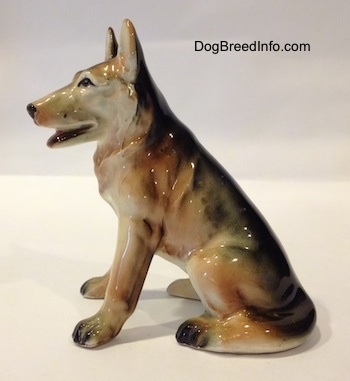 The left side of a ceramic black with tan and white figurine of a sitting German Shepherd. The figurine has detailed black circles for eyes.