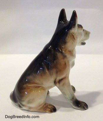 The right side of a figurine of a ceramic sitting German Shepherd. The figurine has long legs.