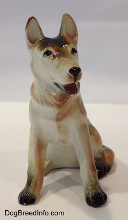 A black with tan and white ceramic German Shepherd sitting figurine. The figurine has its mouth painted open and black circles for eyes.