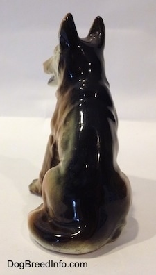 The back of a ceramic figurine of a black with tan sitting German Shepherd. The tail of the figurine wraps around the leg.
