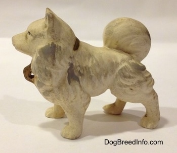 The left side of a ceramic white with gray German Spitz figurine. The figurine has a tail laid on its back.