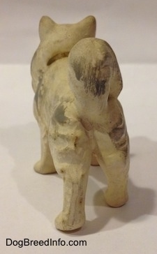 The back of a ceramic figurine of a white with gray German Spitz. The figurine has small hair details along its side.