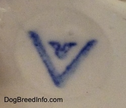 Close up - On the bottom of a figurine stamped on an engraved circle is the logo of a full bee inside of a V logo.