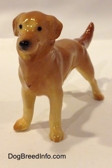 The front left side of a figurine of a brown with tan Golden Retriever. The figurine has black circles for eyes.