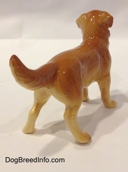 The back right side of a figurine of a brown with tan Golden Retriever. The ears of the figurine are draped on the side of its head.