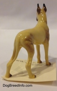 The back right side of a figurine of a tan with black Great Dane figurine. The figurine has long tan legs and small black paws.