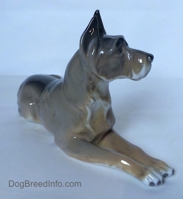 The front right side of a figurine of a Great Dane in a laying down pose. The figurine has fine chest hair details.