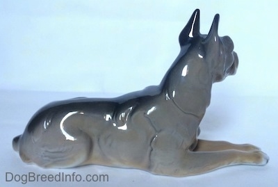 The right side of a black and tan with white figurine of a Great Dane laying down. The figurine has a black strip down its back.