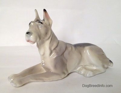 A white with black Great Dane laying down figurine. The figurines face is mostly unpainted.