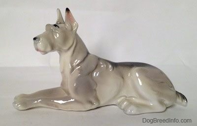 The left side of a white with black Great Dane laying down figurine. The figurine has a long body and a black spot on its back.