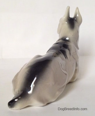 The back right side of a figurine of a Great Dane laying down. The figurine has a short tail that is half black and half white.