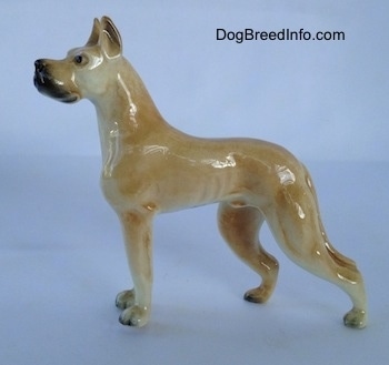 The left side of a tan Great Dane figurine. The figurine has long legs that lead to small paws with black nails.
