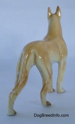 The back right side of a tan Great Dane figurine. The figurine has a long tail attached to its leg.