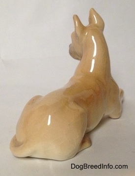 The back right side of a tan Great Dane that is laying down figurine. The figurine has a long body.