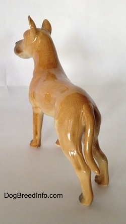 The back left side of a tan Great Dane figurine. The figurine has a long tail and its ears are sticking up.