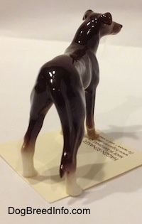 The back right side of a figurine of a brown with white Greyhound. The figurine has a tail that is against its hind leg and it is hard to differentiate from its body.