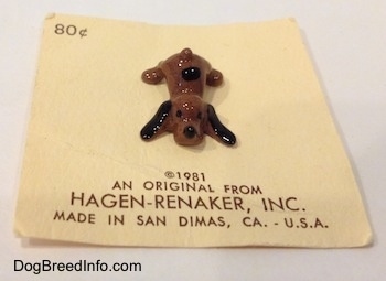 A brown with black Hound Dawg puppy figurine is laying down on a card and it has long black ears.