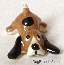 A brown with white and black spotted Hound dog figurine is laying down. The figurine has long black ears laying out.