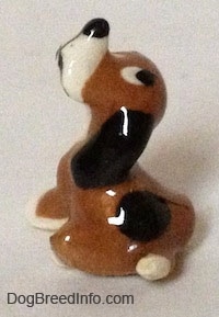 The left side of a brown with white Hound dog sitting figurine with a black spot above its short white tail.