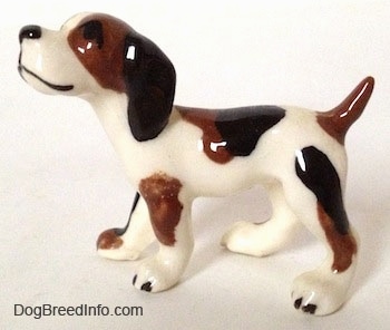 The left side of a white with brown and black vintage Hound dog in a standing pose figurine. The dog has long drop ears, a short docked tail that is up in the air, a black nose and black eyes.