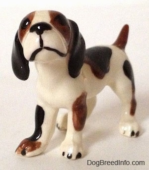 The front left side of a white with brown and black vintage Hound dog figurine. The figurine has long black ears. The nose and mouth are painted black.