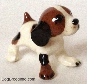 The front right side of a white with brown and black vintage Hound dog figurine with black circles for eyes.