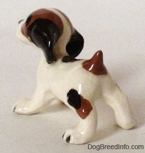 The back left side of a figurine of a white with brown and black Hound dog. All of the figurines have black tipped nails for paws.