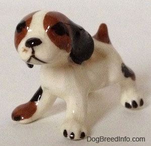 The front left side of a white with brown and black Hound dog figurine that has large black ears attached to the side of its head.
