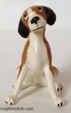 A brown and white with black vintage figurine that is in a sitting pose. The figurines head is tilted to the left and it has long legs with black nails for paws.