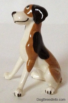 The left side of a figurine of a white and brown with black spots vintage Hound dog. The figurine has a large black spot on its left side.